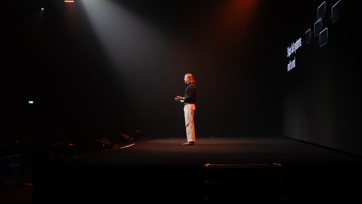 Nick Lafferty presenting at Zero Click London, seen from the side of the stage under a spotlight.